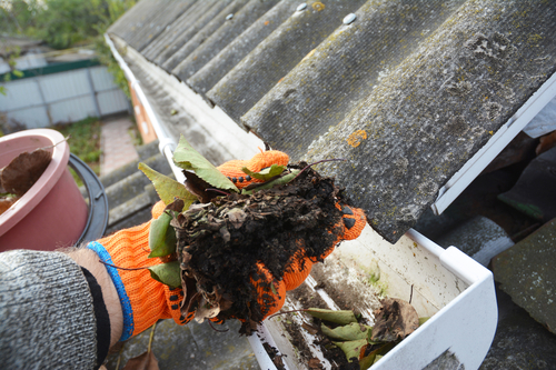 Orange glove on hand removing dirt from gutter